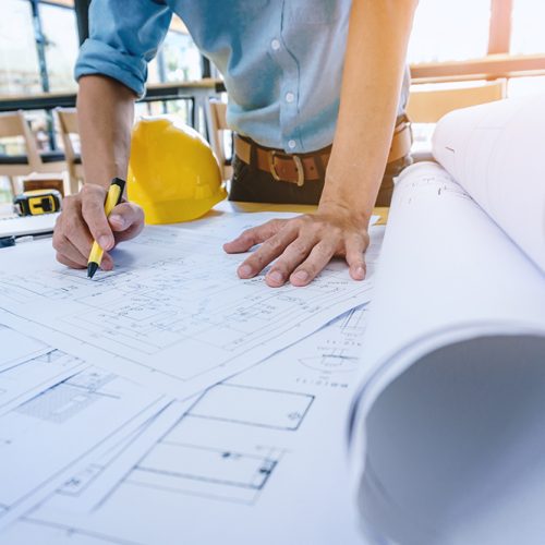 Construction engineer working at blueprint to build large commercial buildings in office. Engineering tools and construction concept.